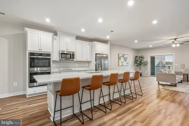 a large kitchen with stainless steel appliances kitchen island granite countertop a refrigerator a stove a dining table and chairs with wooden floor