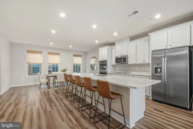 a kitchen with stainless steel appliances granite countertop a refrigerator a sink dishwasher a stove and white cabinets with wooden floor