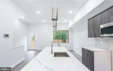 a large white kitchen with granite countertop a stove a sink dishwasher and a microwave oven with white cabinets