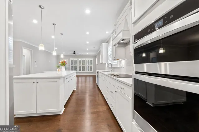 a large white kitchen with a large counter top space a sink stainless steel appliances and cabinets