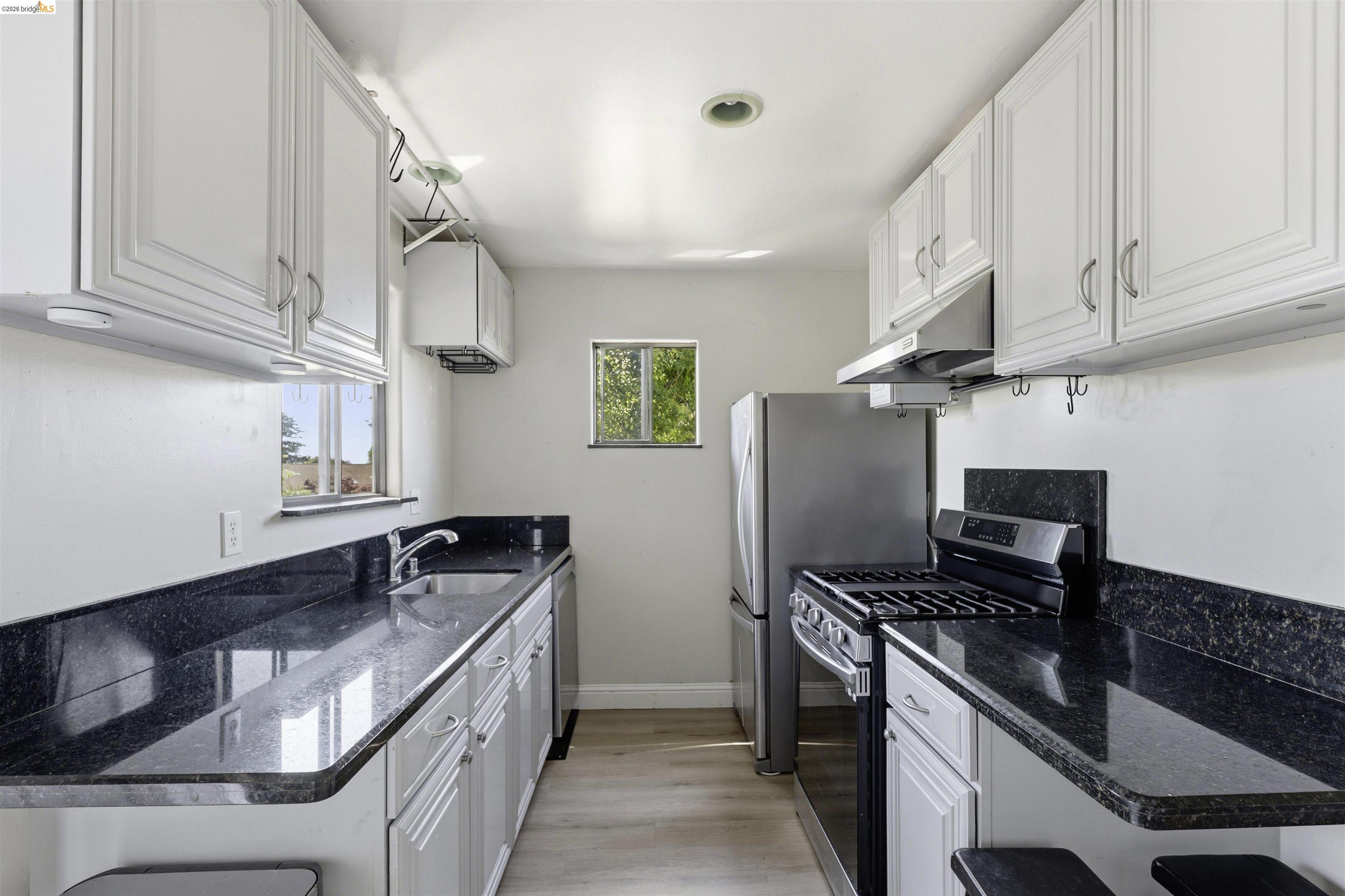 7555 Sunset Way, Unit 6 Aptos, CA 95003 - Photo 15 of 37 Galley kitchen featuring white cabinetry, dark stone countertops, stainless steel appliances, and light wood-finish flooring