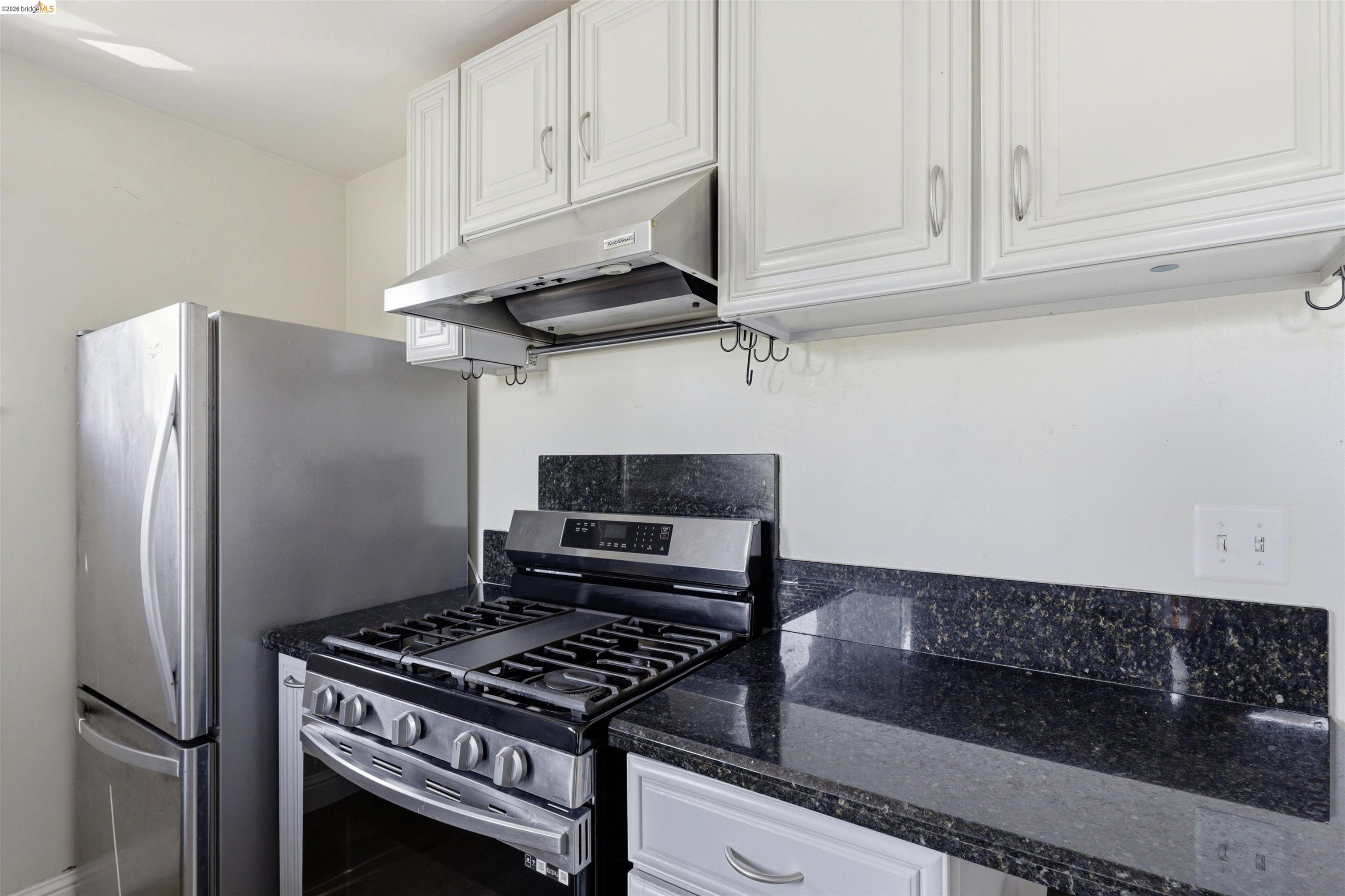 7555 Sunset Way, Unit 6 Aptos, CA 95003 - Photo 16 of 37 Kitchen featuring white cabinetry, stainless steel range with overhead hood, stainless steel refrigerator, and dark speckled countertops