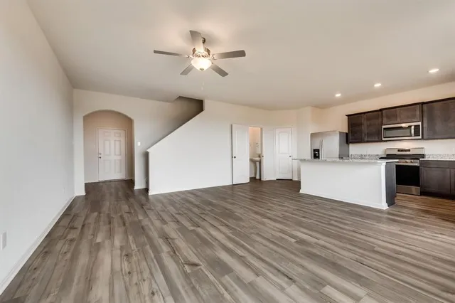 a view of empty room with wooden floor and kitchen view