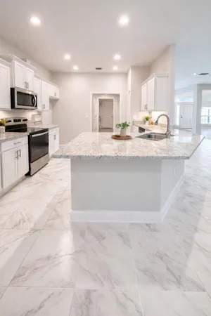 a large white kitchen with kitchen island granite countertop a stove top oven a sink a counter top space and cabinets
