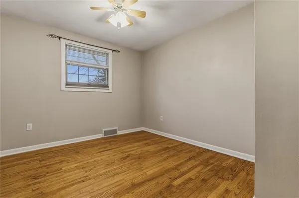 a view of an empty room with wooden floor and a chandelier fan