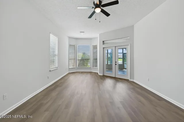 an empty room with wooden floor fan and windows
