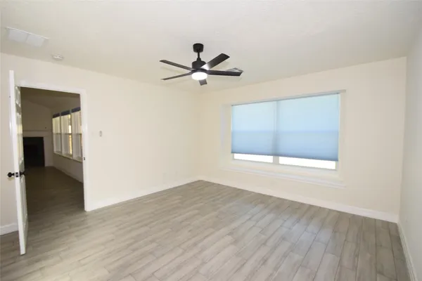 an empty room with wooden floor fan and windows