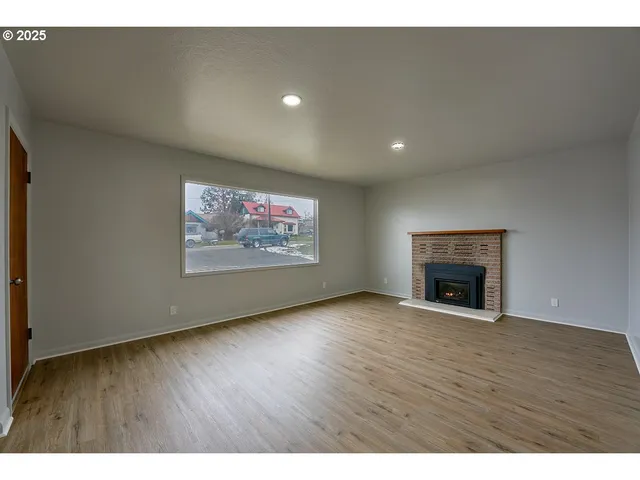 a view of an empty room with wooden floor a fireplace and a window