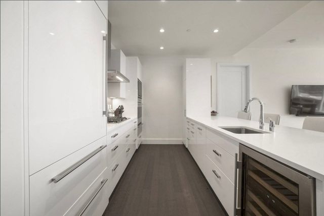 a large white kitchen with a sink and dishwasher a refrigerator with white cabinets