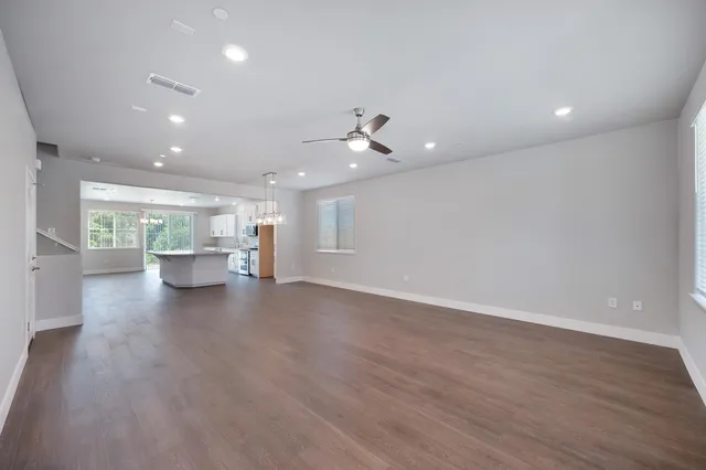a view of an empty room with wooden floor and a kitchen