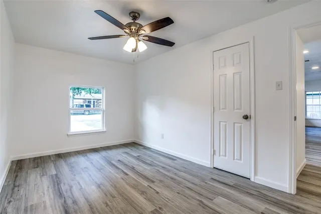 an empty room with wooden floor chandelier fan and windows