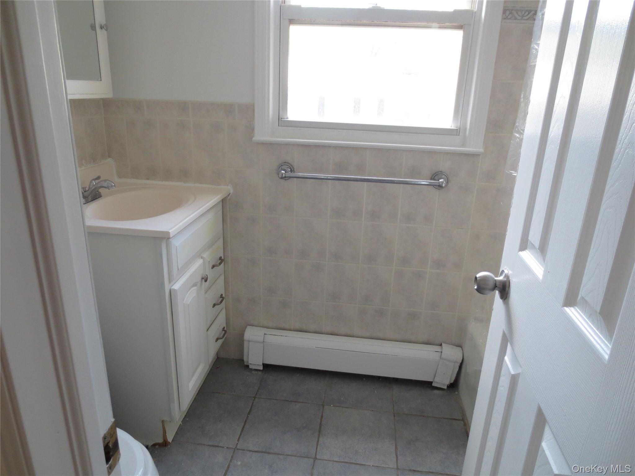 4 Oxford Court, Unit 8007 Suffern, NY 10901 - Photo 10 of 13 Bathroom featuring tile walls, a baseboard radiator, vanity, light tile patterned flooring, and a wainscoted wall