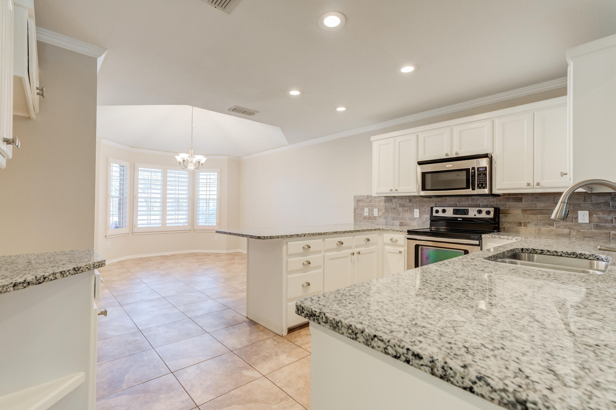 5407 68th Street Lubbock, TX 79424 - Photo 10 of 40 a kitchen with granite countertop a stove a sink and a microwave
