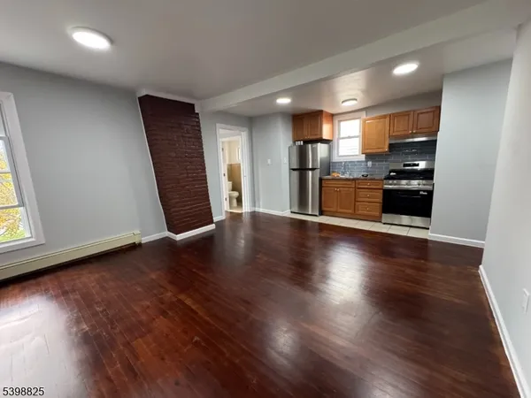 an empty room with wooden floor and entrance to kitchen