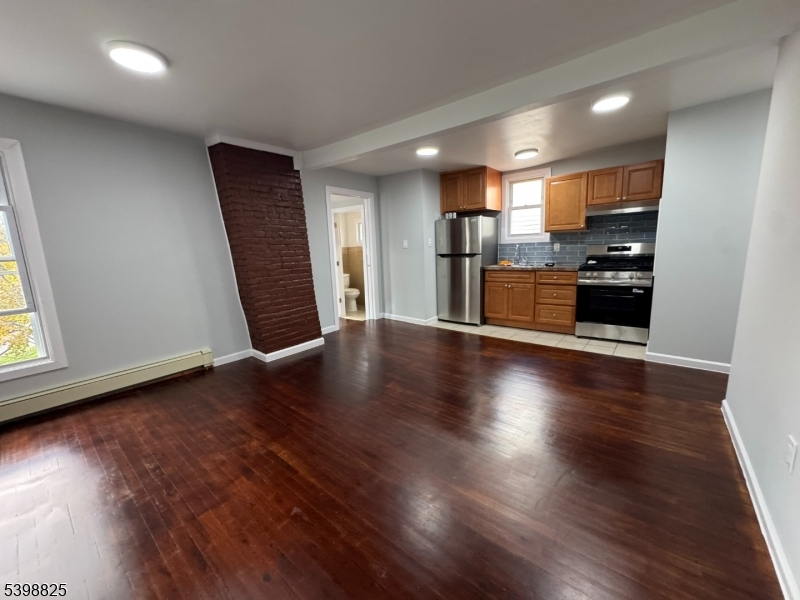 an empty room with wooden floor and entrance to kitchen