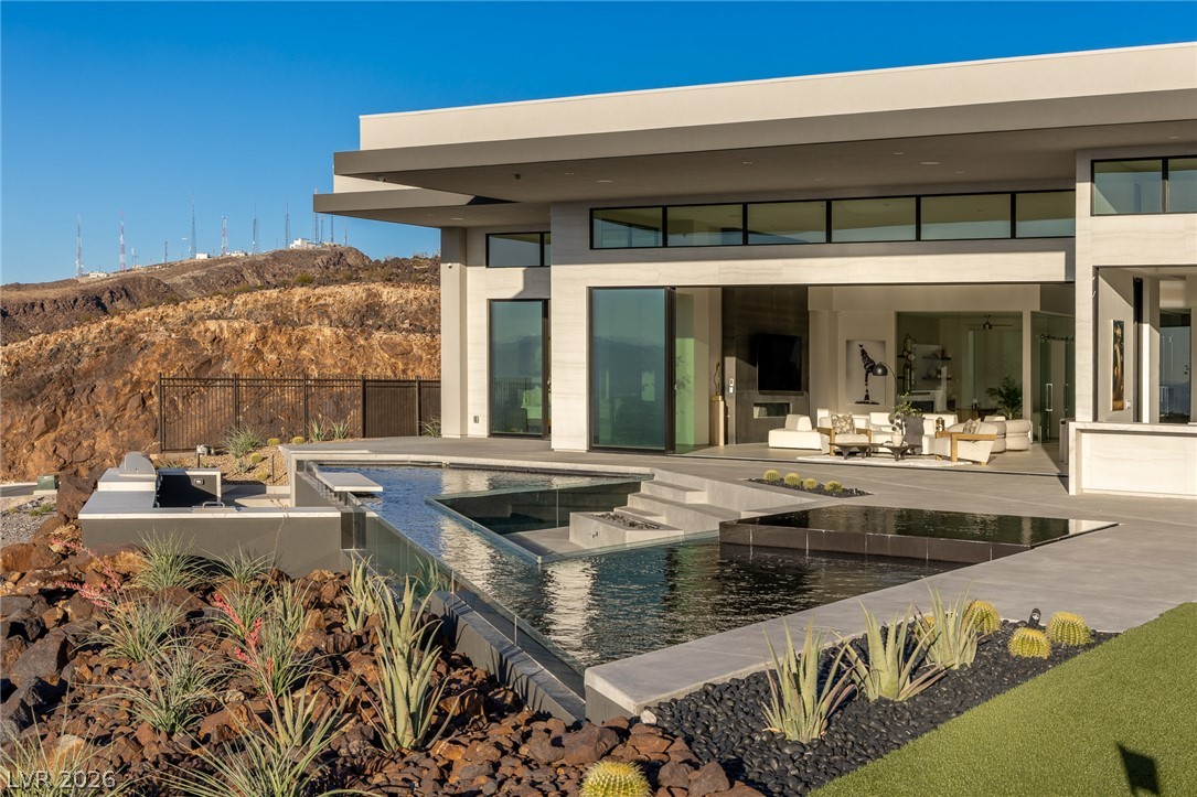 563 Grand Rim Drive Henderson, NV 89012 - Photo 59 of 70 A modern desert oasis showcasing a multi-level pool, outdoor kitchen, and expansive glass doors opening to a hillside vista.