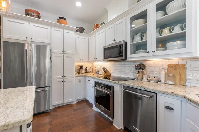 a kitchen with stainless steel appliances granite countertop a refrigerator a stove a sink and white cabinets with wooden floor