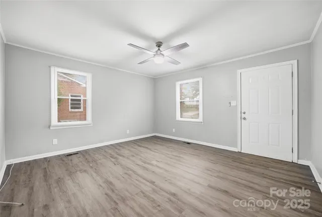 an empty room with wooden floor ceiling fan and windows