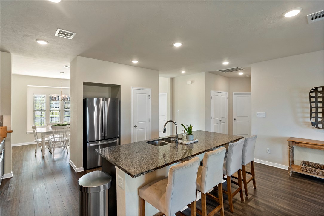1310 Kingsgate Drive Bryan, TX 77807 - Photo 10 of 24 Kitchen featuring dark stone counters, dark wood-style flooring, freestanding refrigerator, recessed lighting, and a kitchen bar