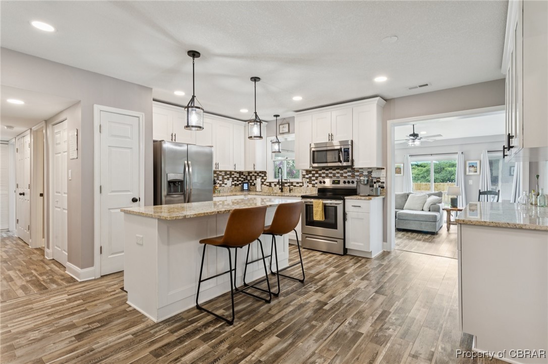 2063 Riley Lane Hayes, VA 23072 - Photo 6 of 35 Kitchen with wood finished floors, stainless steel appliances, white cabinetry, decorative backsplash, and a breakfast bar