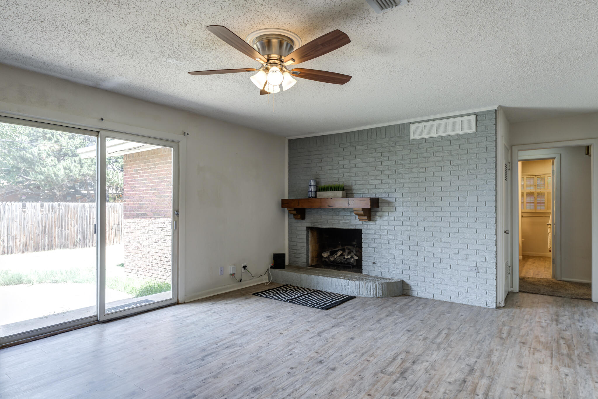 3614 45th Street Lubbock, TX 79413 - Photo 25 of 38 an empty room with windows a fireplace a ceiling fan and wooden floor