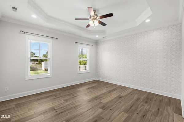 an empty room with wooden floor ceiling fan and windows