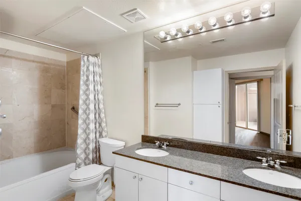 a bathroom with a granite countertop sink a toilet a mirror a bathtub and shower