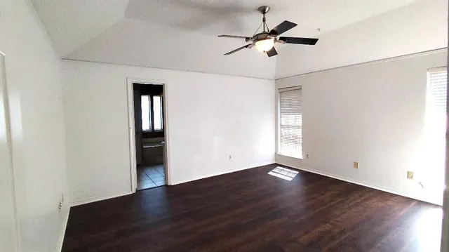 an empty room with wooden floor ceiling fan and windows