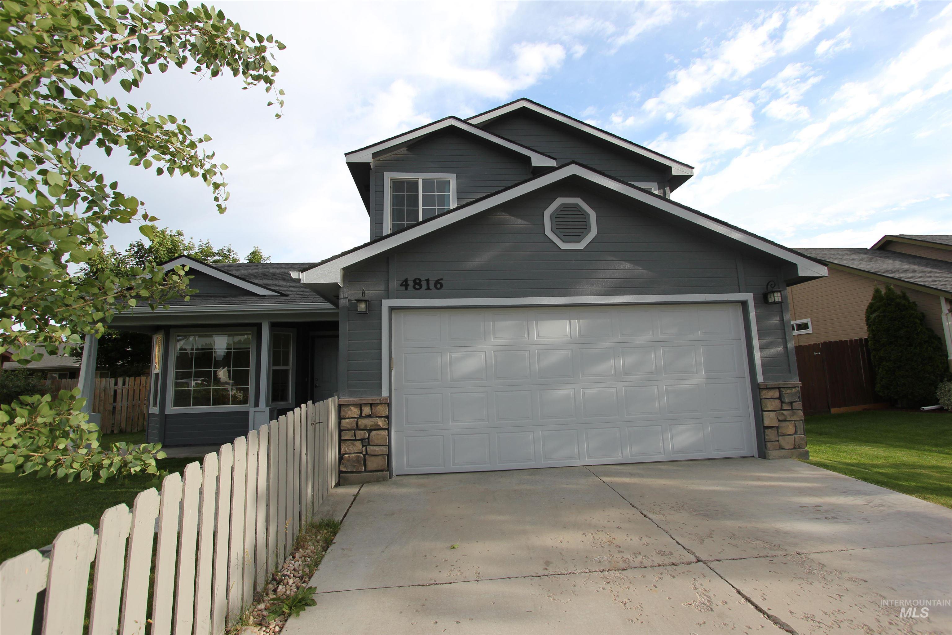 4816 Kadie Street Caldwell, ID 83607 - Photo 1 of 23 Two-story residence featuring gray siding, a two-car garage with panel door, stone column accents, and a white picket fence
