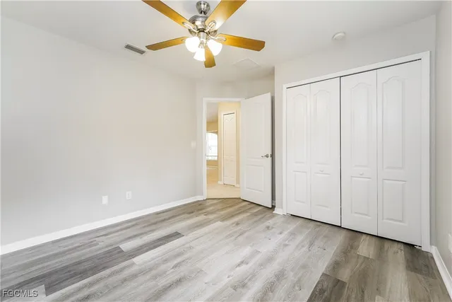 an empty room with wooden floor closet fan and windows