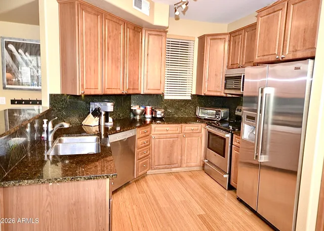 a kitchen with granite countertop a refrigerator a sink dishwasher stove and white cabinets with wooden floor