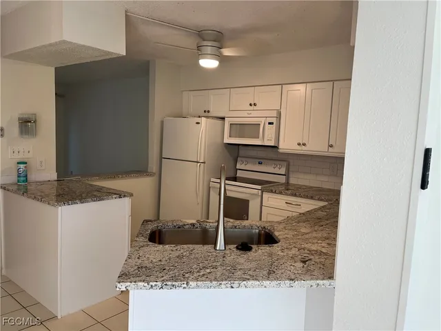 a kitchen with granite countertop a refrigerator a stove a sink and white cabinets