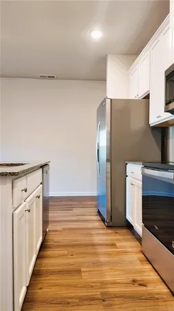 a view of an empty room with wooden floor and a kitchen