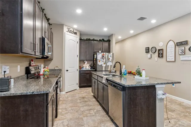 a kitchen with stainless steel appliances kitchen island granite countertop a refrigerator a stove a sink dishwasher and a dining table with wooden floor