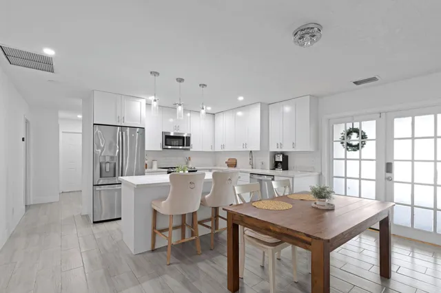 a kitchen with stainless steel appliances granite countertop a table chairs wooden floors and white cabinets