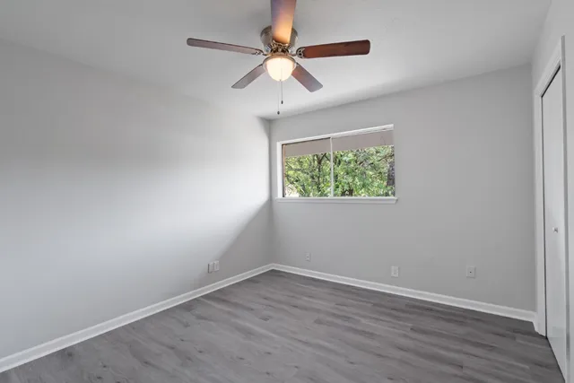 an empty room with wooden floor ceiling fan and windows