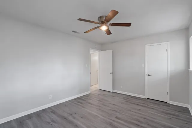 an empty room with wooden floor ceiling fan and windows