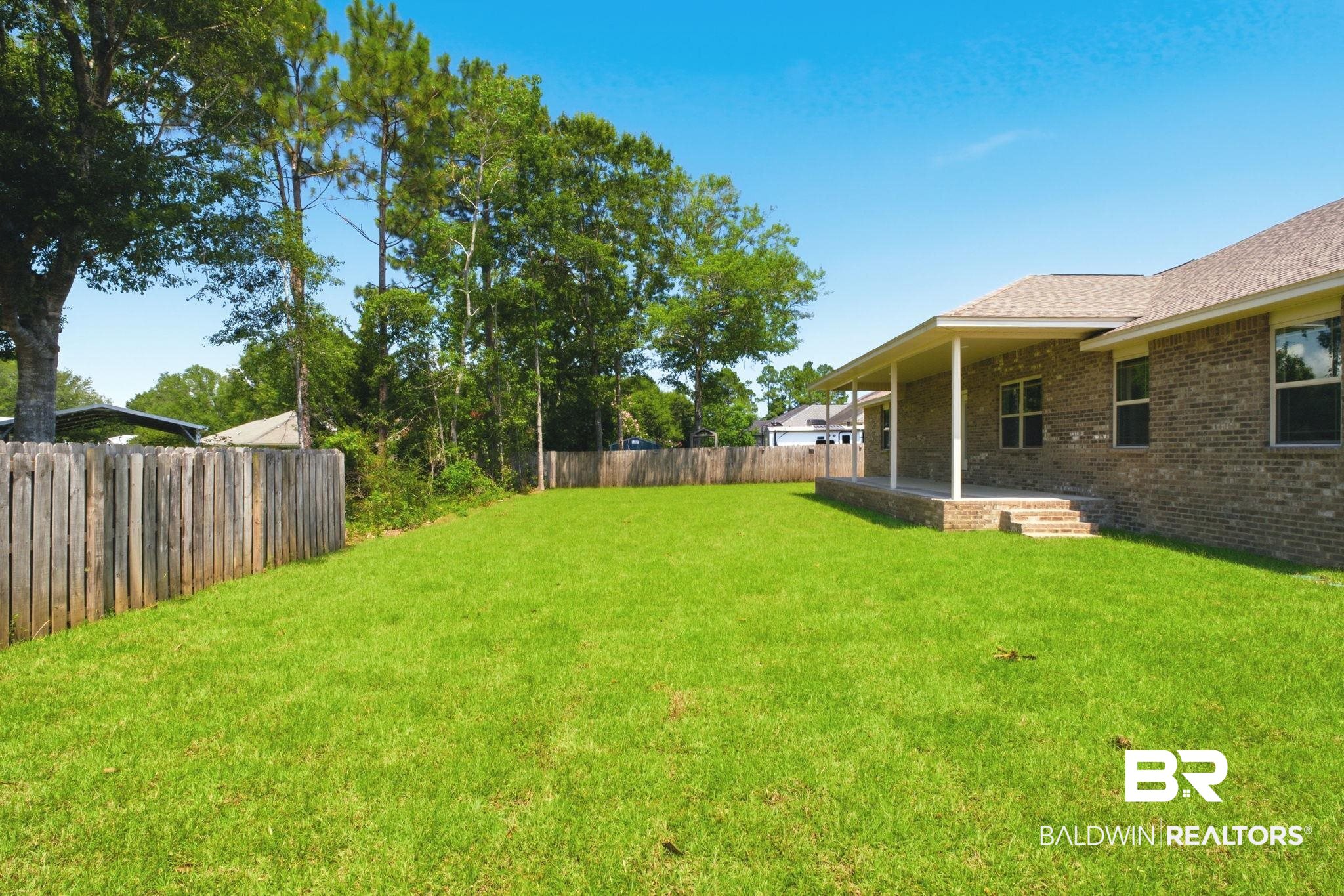 32656 Arbor Ridge Circle Lillian, AL 36549 - Photo 36 of 56 Expansive backyard featuring a lush green lawn, full privacy fencing, and a covered patio with brick steps