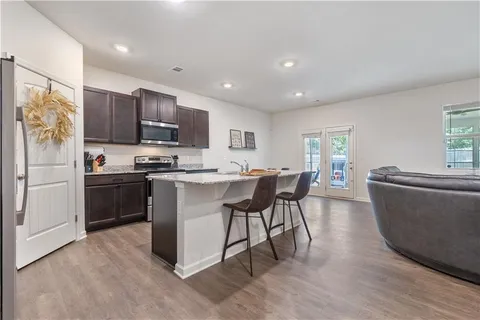 a kitchen with stainless steel appliances kitchen island granite countertop a refrigerator a stove a sink a dining table and chairs with wooden floor