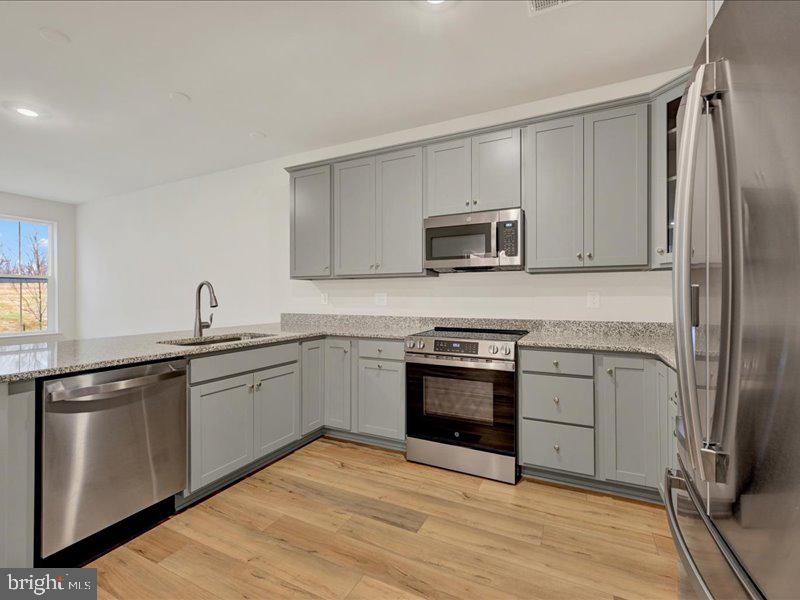 4003 Seaside Alder Road, Unit 102 ASTER Bowie, MD 20720 - Photo 6 of 27 a kitchen with stainless steel appliances granite countertop a stove top oven a sink and dishwasher a refrigerator with wooden floor
