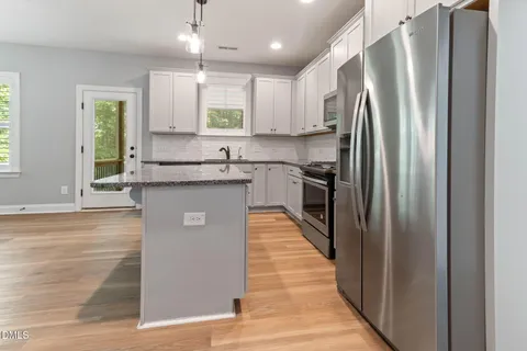 a kitchen with stainless steel appliances granite countertop a refrigerator a sink dishwasher a stove and white countertops with wooden floor