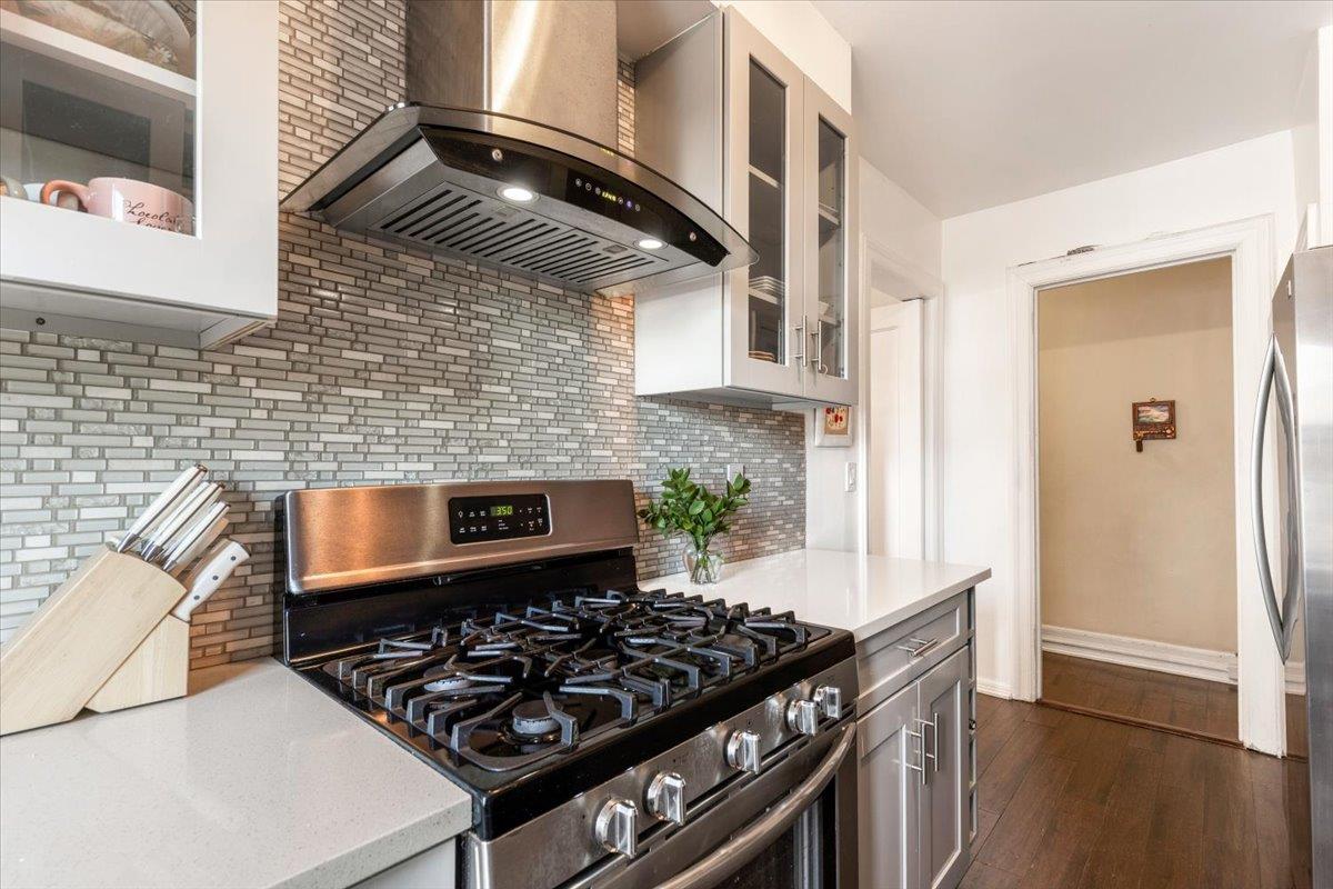 56 Sagamore Road, Unit 2A Bronxville, NY 10708 - Photo 1 of 1 Kitchen with decorative back splash, glass insert cabinets, stainless steel appliances, light countertops, and wall chimney range hood