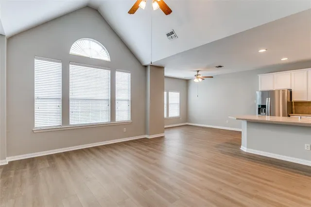 an empty room with wooden floor chandelier fan and windows