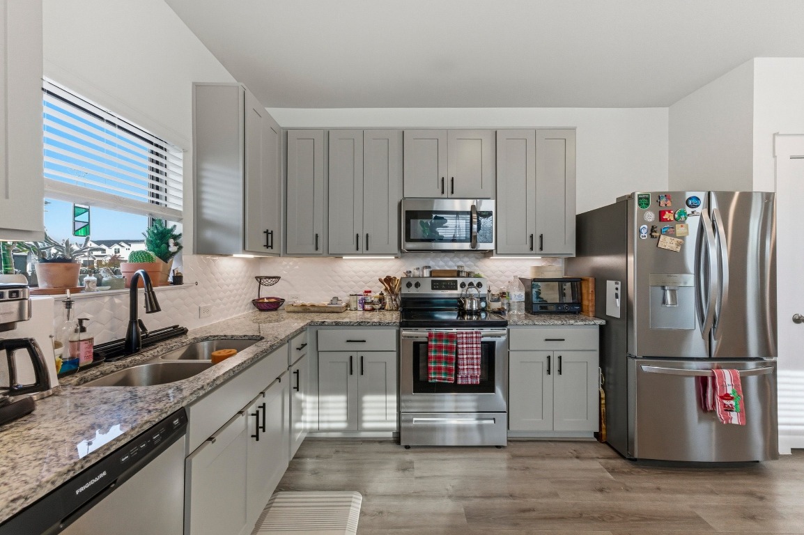 159 Threshing Road, Unit A Buda, TX 78610 - Photo 11 of 33 Kitchen with stainless steel appliances, light stone counters, gray cabinetry, and light wood-style floors