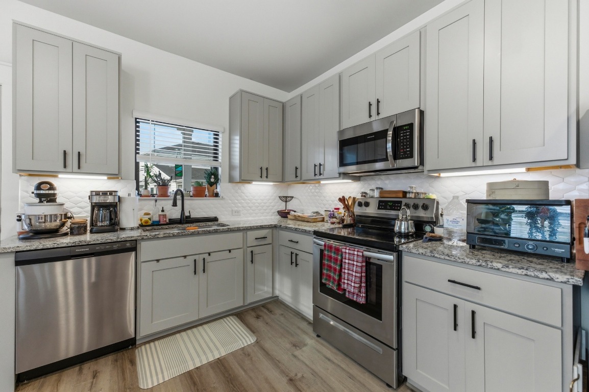 159 Threshing Road, Unit A Buda, TX 78610 - Photo 12 of 33 Kitchen with stainless steel appliances, gray cabinetry, light stone counters, light wood-style flooring, and backsplash