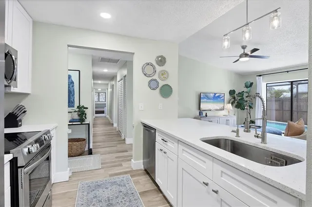 a large white kitchen with a stove a sink a refrigerator and a living room