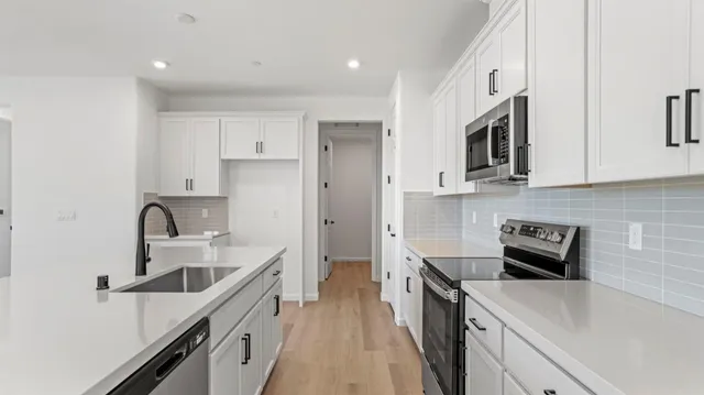 a kitchen with a sink dishwasher stove and white cabinets with wooden floor