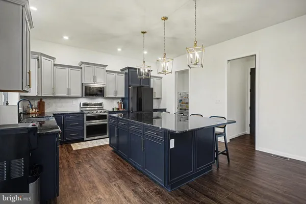 a kitchen with kitchen island granite countertop a stove top oven a sink dishwasher a refrigerator and a dining table with wooden floor