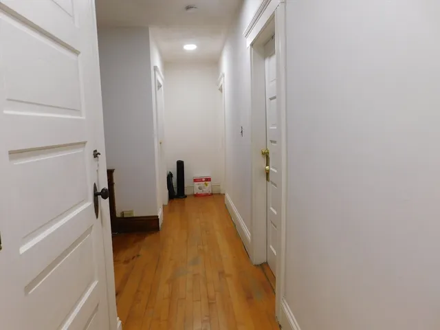 a view of a hallway with wooden floor and a bathroom