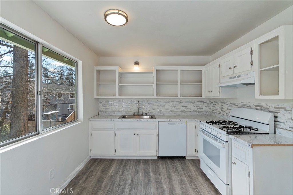 a kitchen with granite countertop a stove a sink dishwasher and white cabinets with wooden floor
